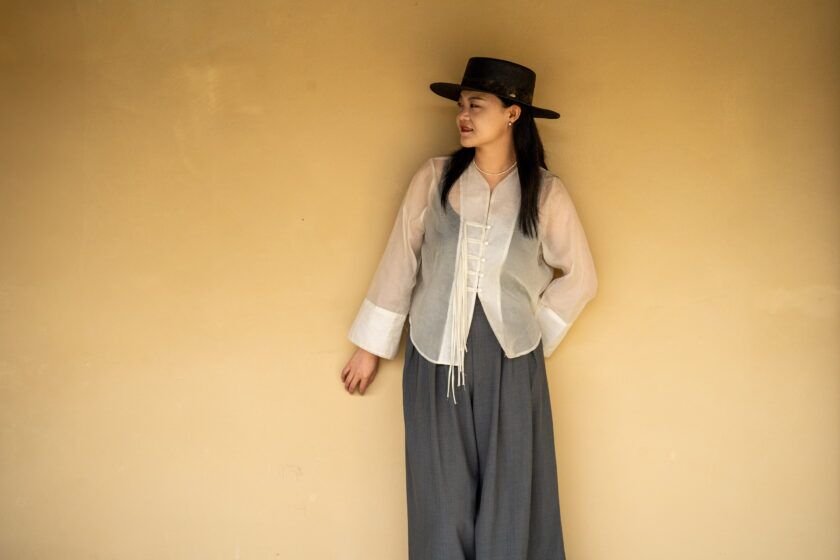 Sheer ivory organza jacket with corded frog closures, grey wide-leg trousers and black wide-brim hat, worn by a model