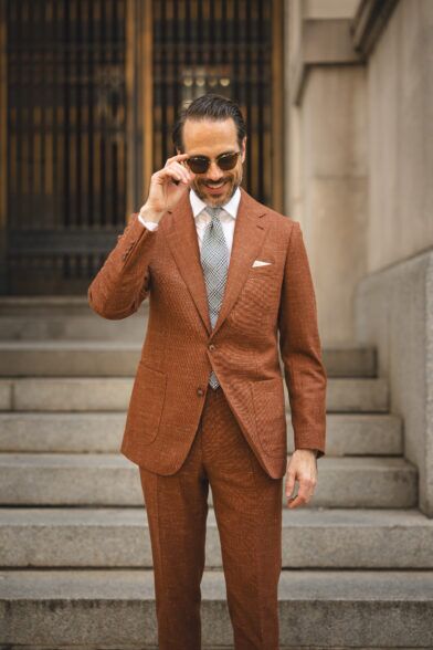 Terracotta textured linen-blend suit with white shirt and grey checked tie, worn by a model on stone steps