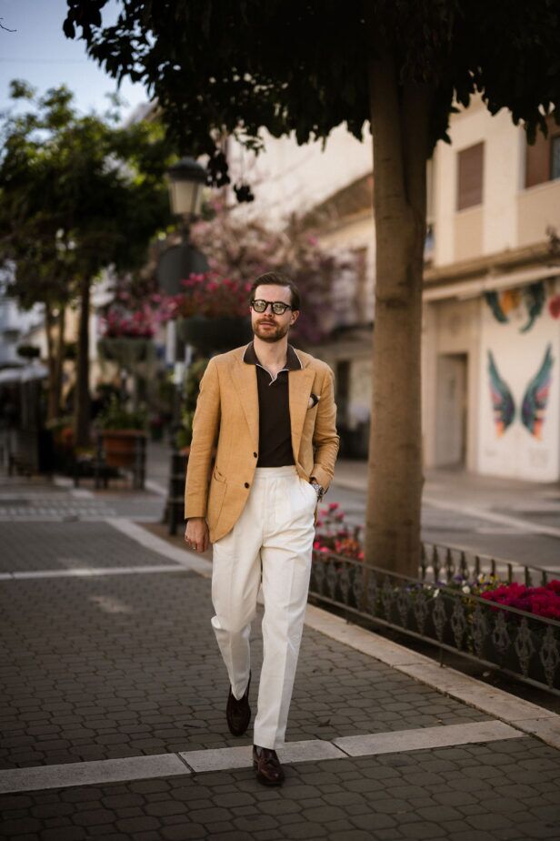 Tan linen sport coat with brown tipped polo, cream trousers and burgundy tassel loafers, worn by a model on a street