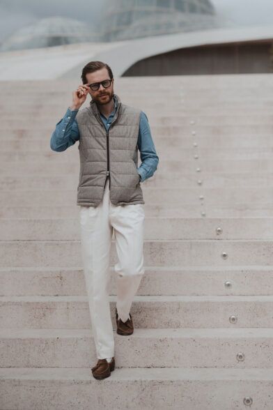 Grey quilted wool zip vest with blue chambray shirt, cream trousers and brown suede loafers, worn by a model on steps