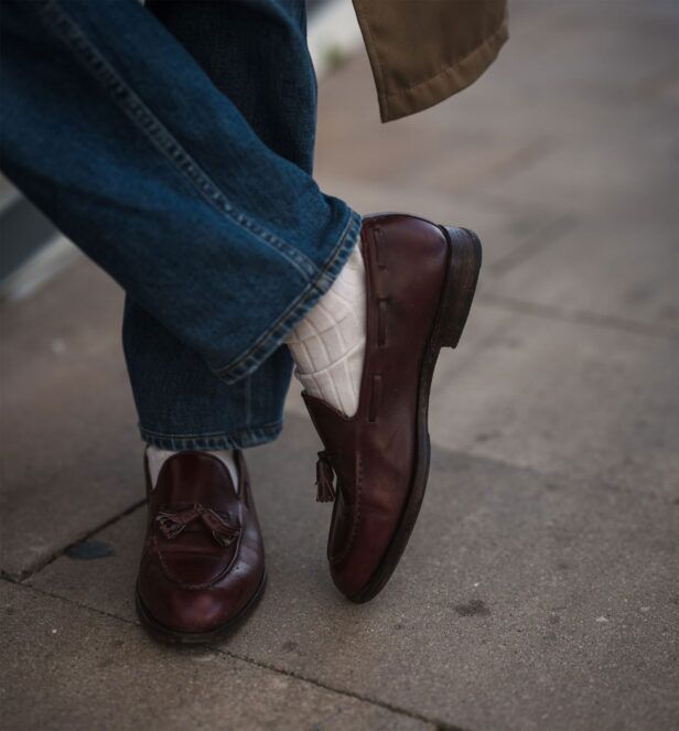 Burgundy leather tassel loafers with cream socks and dark denim jeans, a close-up of the feet
