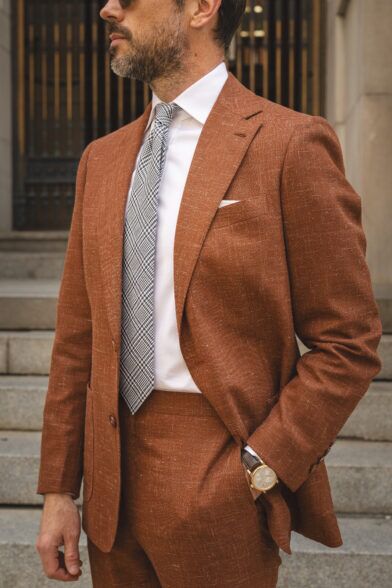 Terracotta textured linen-blend suit with white shirt and black check tie, worn by a model
