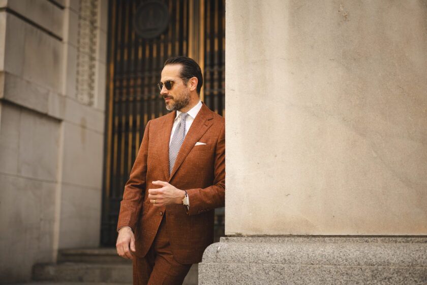 Terracotta textured linen-look suit with white shirt, navy check tie and white pocket square, worn by a model outdoors