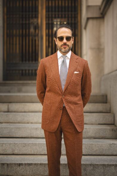 Terracotta textured linen-blend suit with white shirt, black and white check tie and pocket square, worn by a model
