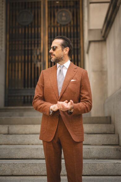 Terracotta textured linen-blend suit with white shirt, checked tie and white pocket square, worn by a model