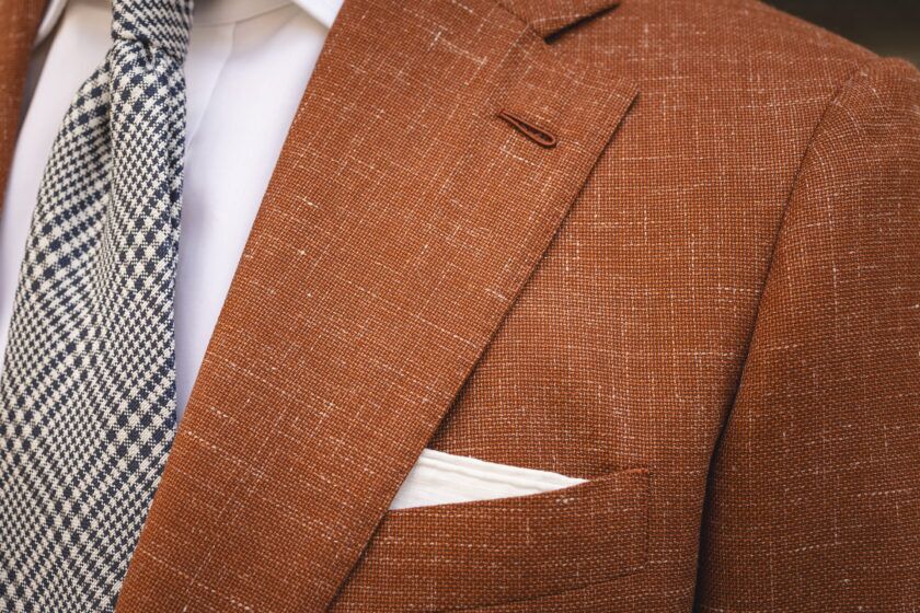 Terracotta textured wool sport coat with notch lapel, white shirt, navy check tie and white pocket square, close-up detail