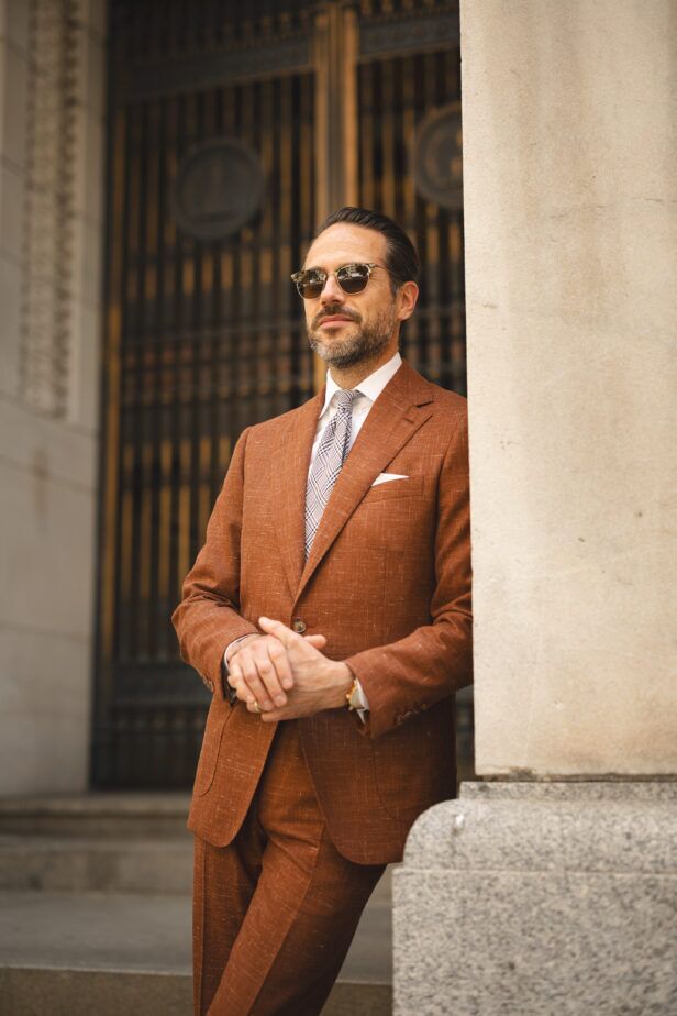 Terracotta linen-blend suit with white shirt, checked tie and white pocket square, worn by a model outdoors