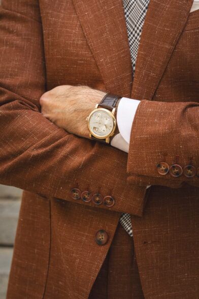 Terracotta textured linen-blend sport coat with horn buttons, gold watch on brown leather strap, a close-up detail
