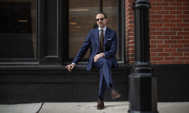 Royal blue two-piece suit with light blue shirt, brown knit tie and brown brogues, worn by a model on a city street