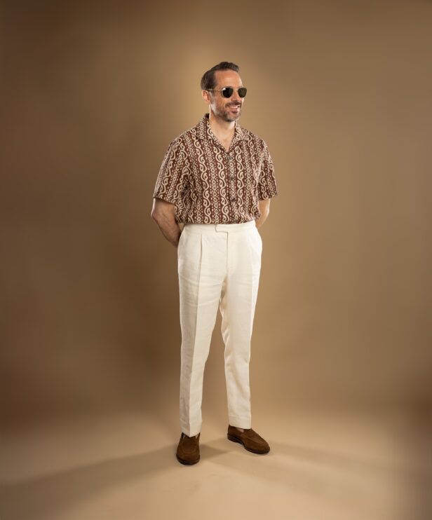 Brown and cream printed camp collar shirt with cream pleated linen trousers and suede loafers, worn by a model