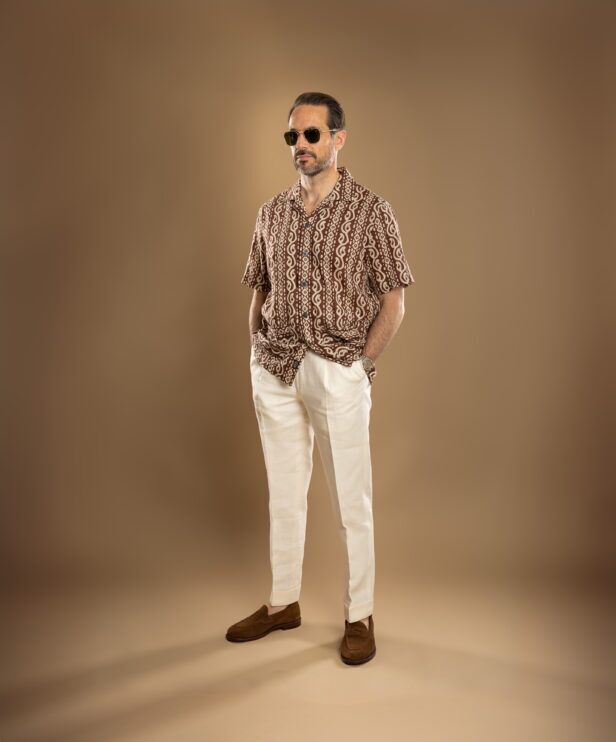 Brown and cream printed camp collar short sleeve shirt with ivory linen trousers and suede loafers, worn by a model