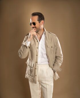 Tan linen safari jacket with patch pockets, white shirt and cream trousers, worn by a model