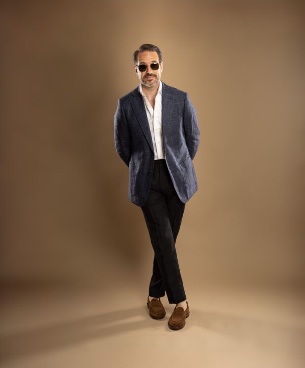 Blue checked linen sport coat with white shirt, black trousers and brown suede loafers, worn by a model