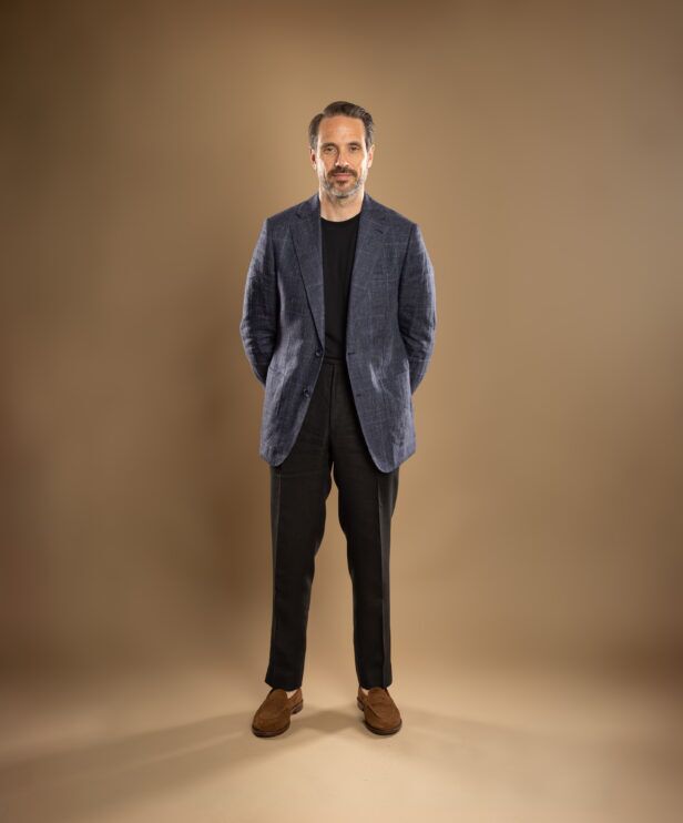 Blue checked linen sport coat with black t-shirt, dark brown trousers and tan suede loafers, worn by a model