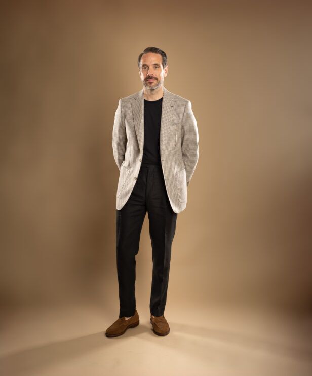 Cream and tan houndstooth sport coat with black t-shirt, charcoal trousers and brown suede loafers, worn by a model