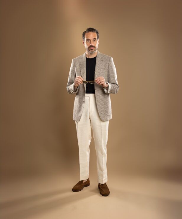 Tan houndstooth sport coat with black t-shirt, cream linen trousers and brown suede loafers, worn by a model