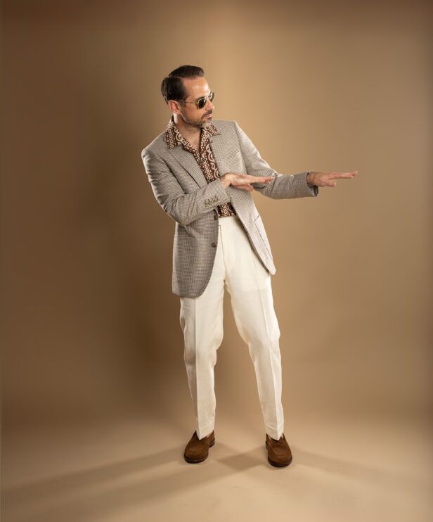 Tan houndstooth check sport coat with brown printed camp shirt, cream trousers and suede loafers, worn by a model