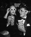 Couple in 1950s evening dress wearing 3D glasses and holding popcorn in a cinema, archive black and white photo