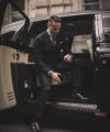 Navy double-breasted suit with striped shirt and green medallion tie, worn by a model stepping from a car