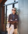 Brown flannel safari jacket over a grey polo with cream trousers, arms crossed