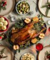 Roast goose on a platter surrounded by festive side dishes and red wine