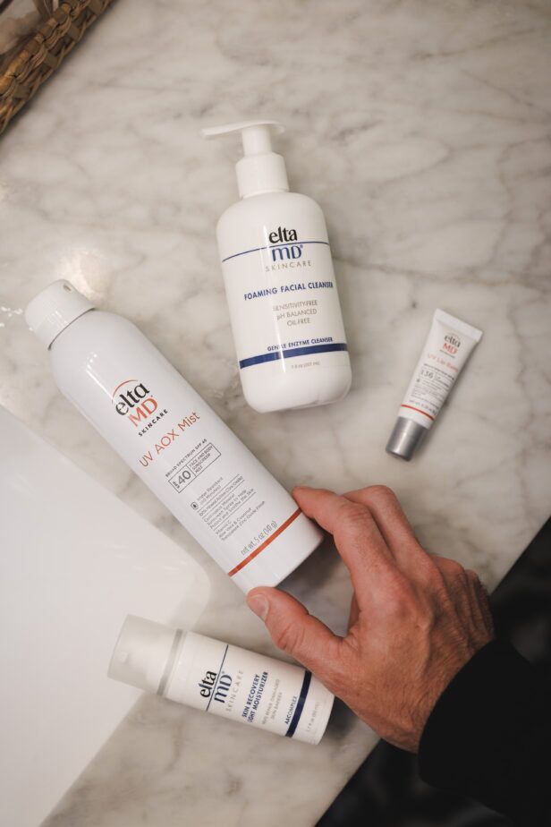 Skincare bottles on a marble vanity beside a leather wash bag and a mirror