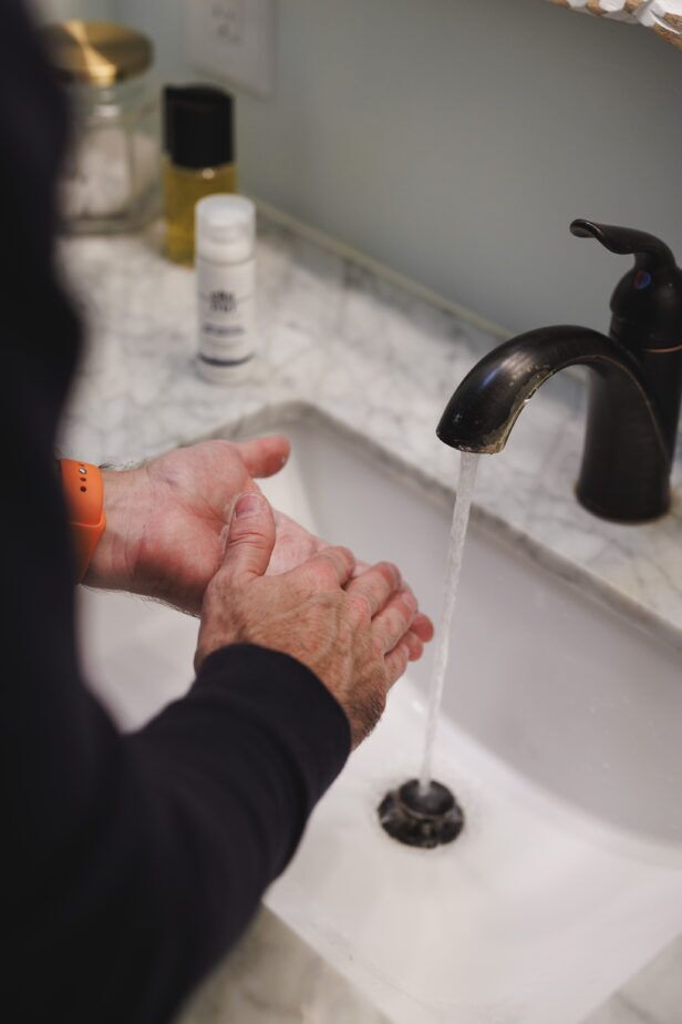 Pump bottle of foaming facial cleanser held in both hands above a sink