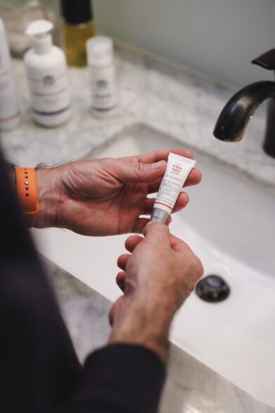 Small tube of UV lip balm held in both hands above a marble bathroom sink