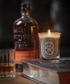 Lit Feu de Bois candle on a book beside a whisky bottle and a cut glass tumbler