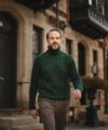 Green cable-knit turtleneck sweater with brown tweed trousers, worn by a model