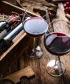 Red wine bottles in a wooden gift crate beside two filled glasses on a rustic table, a lifestyle scene