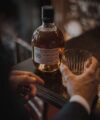 Glenrothes 36 year whisky bottle and a cut glass tumbler held at a dark bar