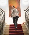 Cream houndstooth sport coat with dark trousers, worn by a model climbing a red-carpeted staircase, back view