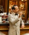 Cream dinner jacket with a black bow tie, worn by a model raising a whisky at a bar