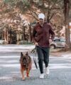 Burgundy hooded fleece jacket with dark joggers and white sneakers, worn by a man walking a dog