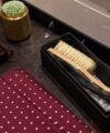 Burgundy dotted pocket square beside a boxed clothes brush and a leather valet tray