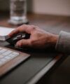 Grey shirt cuff at a hand resting on a wireless mouse beside a keyboard