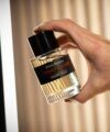 French Lover eau de parfum in a clear bottle with a black cap, held in one hand