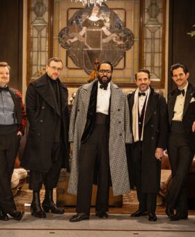 Five guests in tartan, houndstooth, velvet and black tie, a group portrait by stone urns