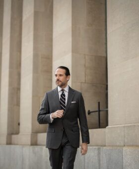 Charcoal grey suit with a white shirt and striped tie, worn by a model walking