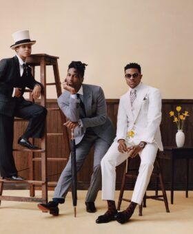 Three people in pinstripe, grey and cream suits posed around a wooden ladder