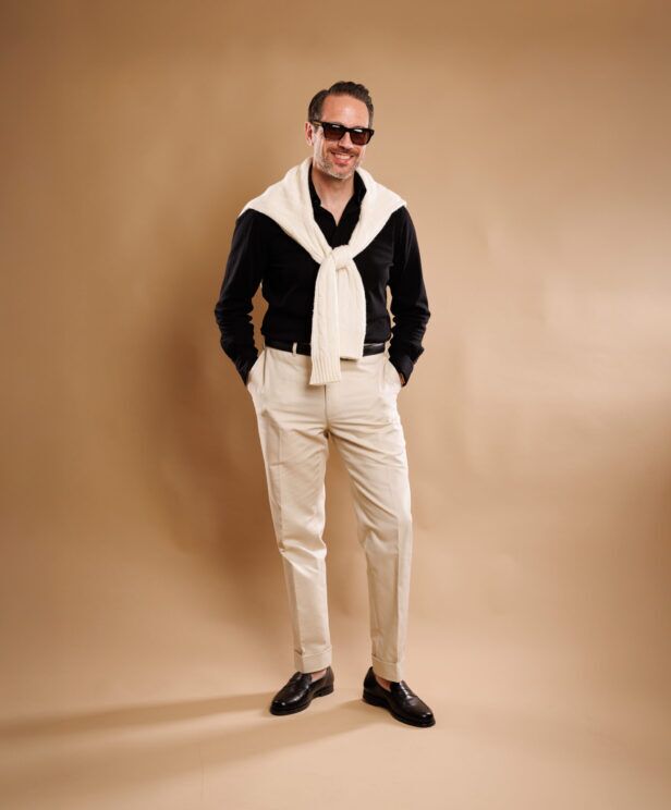 Black button-up with cream sweater, stone chinos and brown loafers, worn by a model