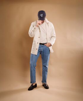 Natural cotton canvas chore coat over a tee with jeans and a navy cap, full length