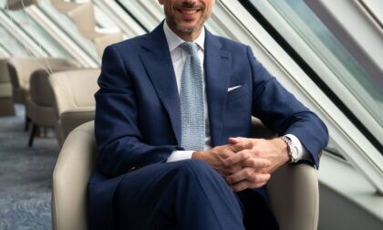 Royal blue birdseye suit with white shirt and pale blue knit tie, worn by a seated model