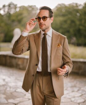 Tan solaro suit with white shirt and brown knit tie, worn by a model on a stone terrace
