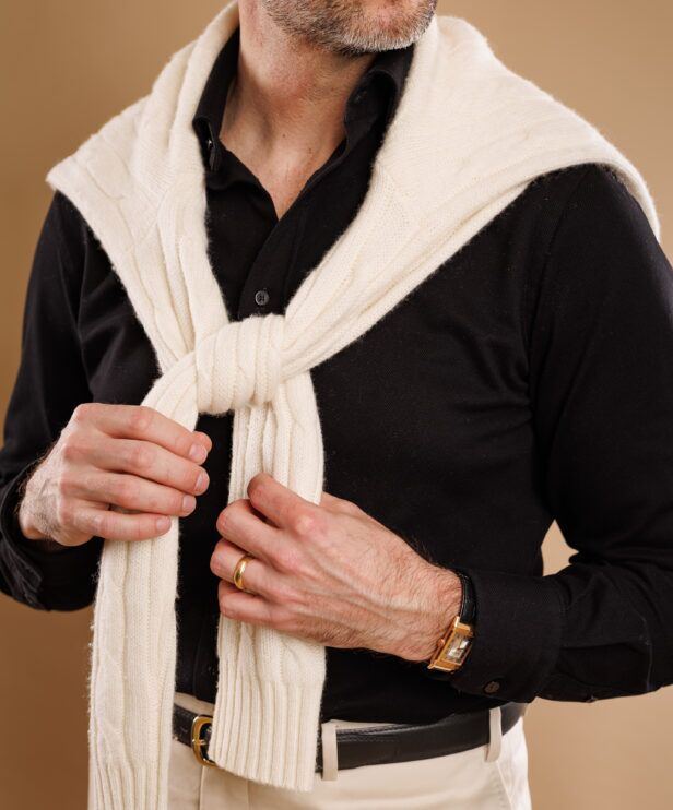 Cream cable sweater knotted over a black knit polo, a close-up of the shoulders and belt