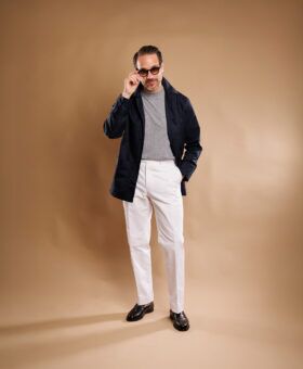 Navy cotton chore coat over a grey sweater with white trousers, worn by a model