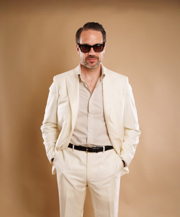 Ivory suit with a chambray shirt and black belt, worn by a model against a tan backdrop