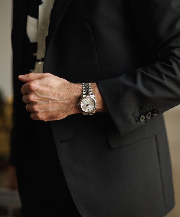 Black tropical wool suit with a steel watch at the cuff, a close-up of the sleeve and pocket