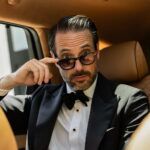 Black peak lapel tuxedo with bow tie and stud front shirt, worn by a model in a car